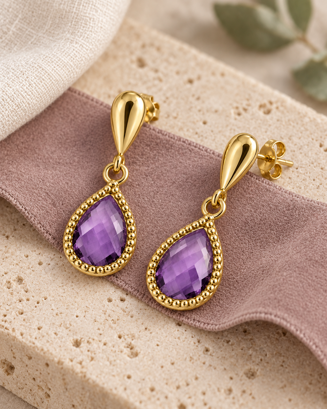 Boucles d’oreilles améthyste posées à plat sur un ruban mauve et du travertin